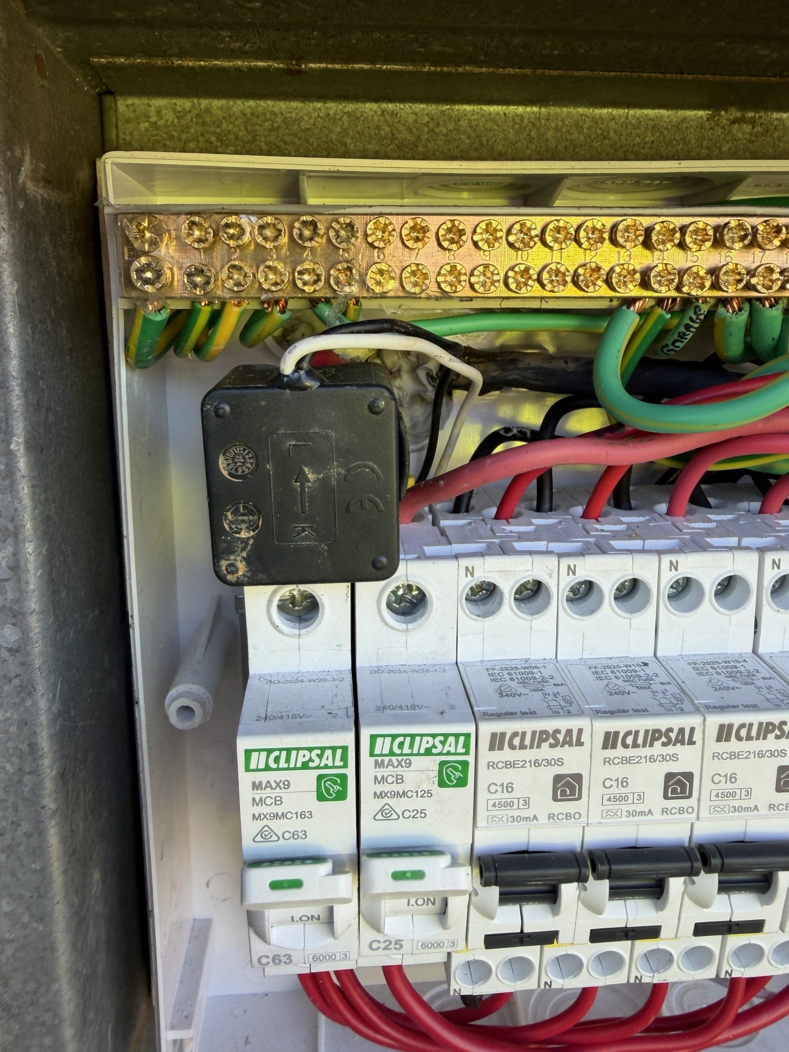 Real installation photograph of a black grid CT clamped around the main active conductor inside a switchboard.
