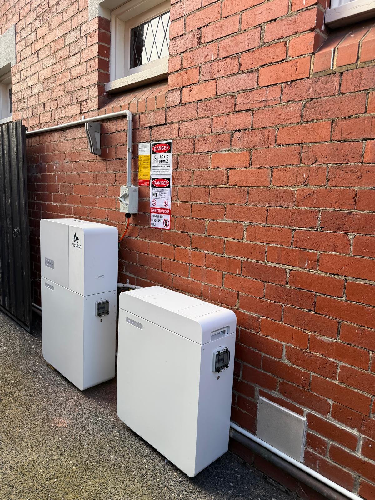 Real AlphaESS installation by Maxim Energy: two battery units arranged side by side against a brick wall